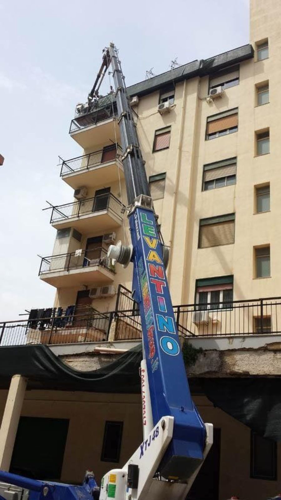 Una gru che si estende verso l'alto fino al balcone di un edificio, probabilmente per lavori di riparazione o costruzione.