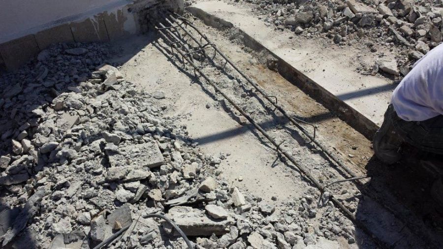Cantiere: la demolizione del calcestruzzo rivela l'armatura in barre. I detriti circondano una sezione parzialmente rimossa.