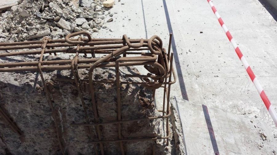 Armatura esposta che sporge da una struttura in cemento in un cantiere con barriera a strisce rosse e bianche.