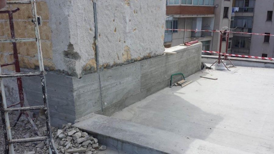 Lavori di costruzione di un tetto: riparazione di un muro di cemento vicino a un edificio alto. Presenza di ponteggi, detriti e attrezzi.