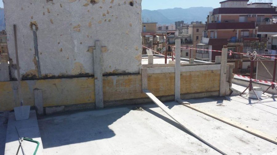 Cantiere con casseforme e supporti in cemento su un tetto. Luce solare intensa.