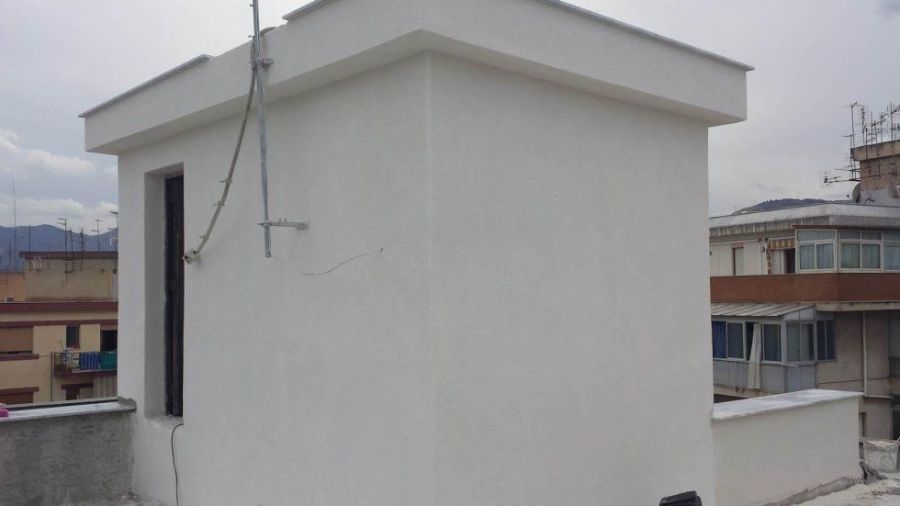 Edificio bianco con una piccola finestra e un'antenna sul tetto che domina altri edifici.