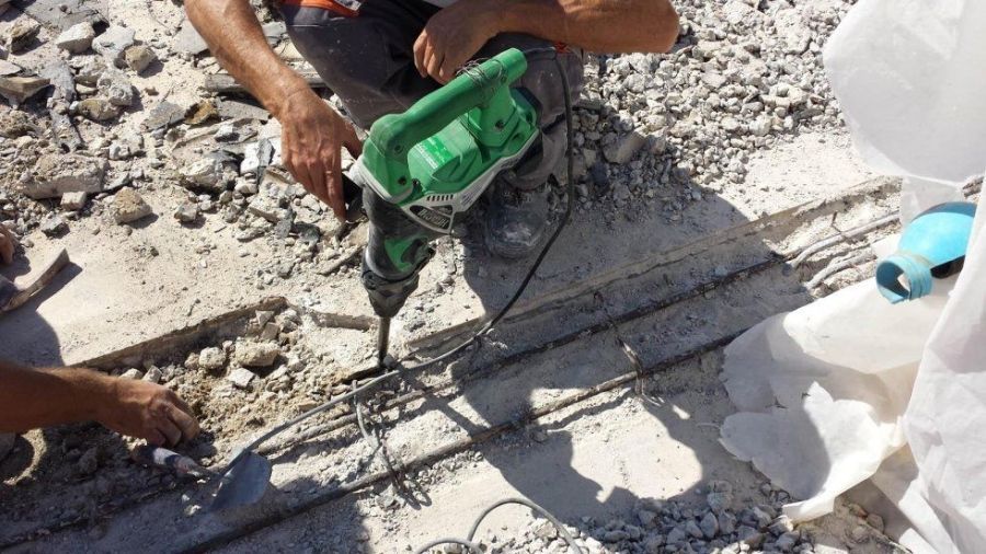 Persona che usa un trapano elettrico ecologico sul cemento. Le barre d'armatura sono esposte. Cantiere edile.