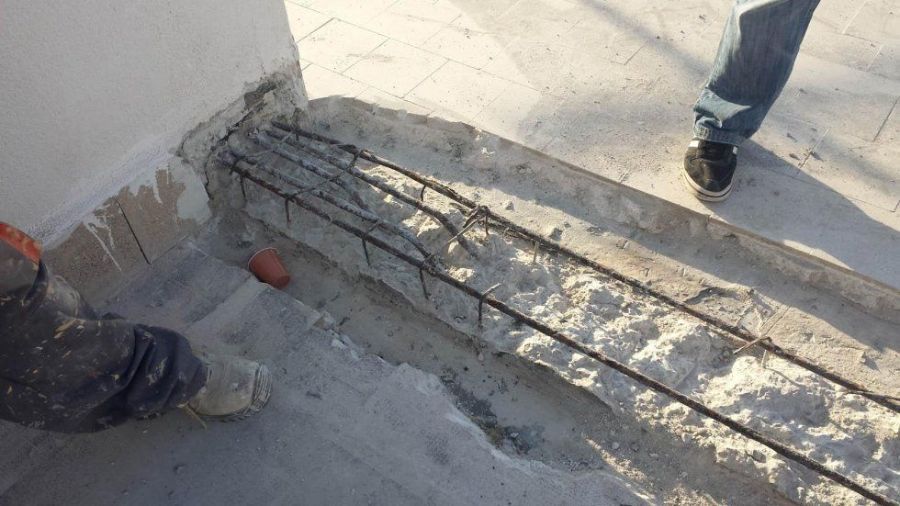 Lavori in calcestruzzo: barre di armatura esposte in una trincea. Gambe e piedi di una persona sono visibili sul bordo.