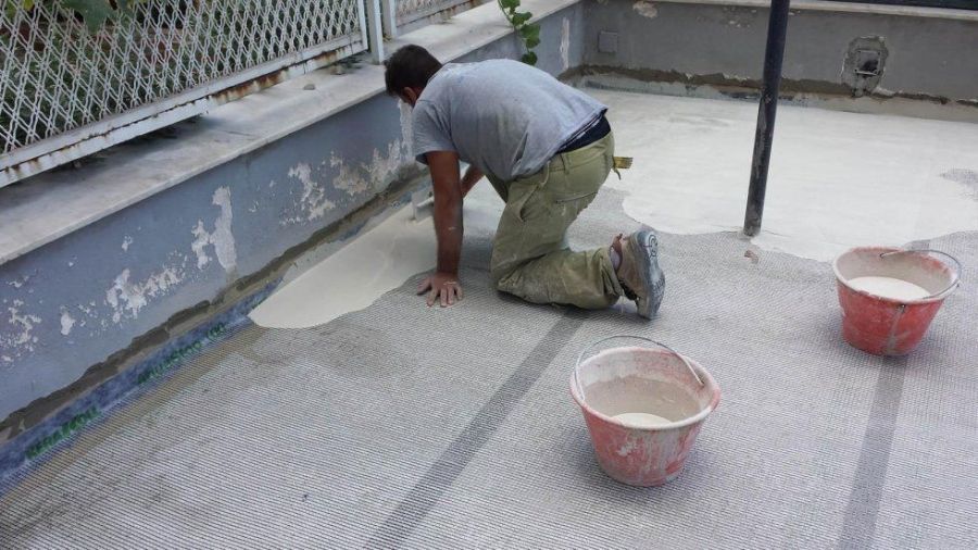 Una persona è inginocchiata su un patio e sta stendendo una vernice chiara. Due secchi rossi sono lì vicino.