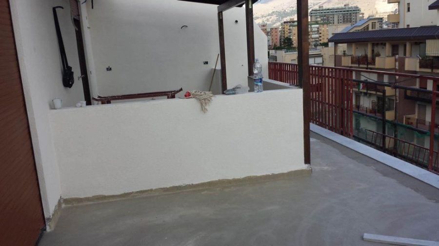 Balcone con pareti bianche, ringhiera rossa e vista su edifici e montagne.
