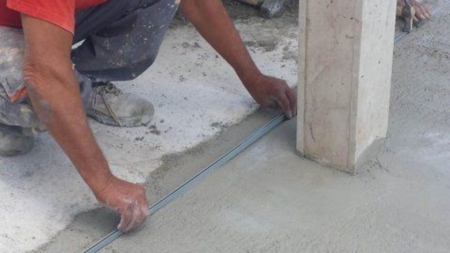 Persona che utilizza una livella per lisciare il calcestruzzo fresco attorno a un pilastro all'aperto.