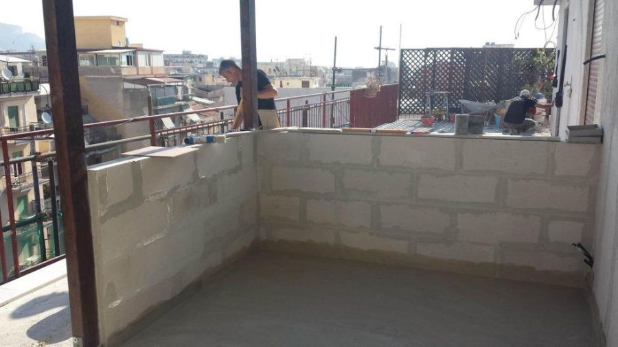 Uomo che lavora su un tetto con pareti in mattoni e ringhiera, con vista sulla città.