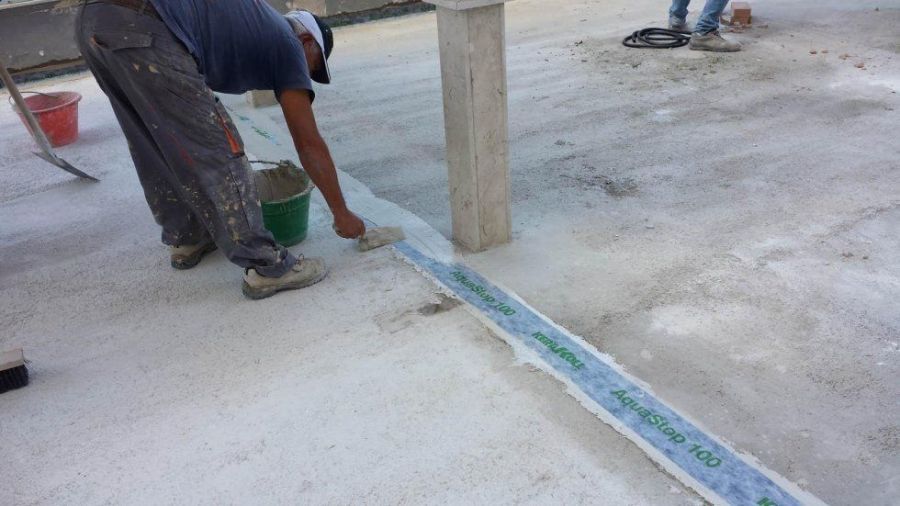 Operaio edile che applica il sigillante a un giunto su una superficie di cemento bianco, vicino a una colonna di sostegno.