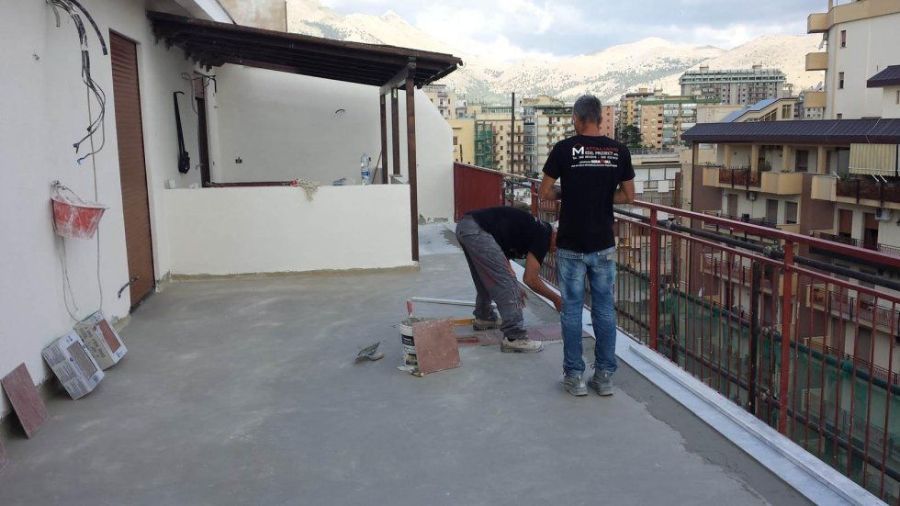 Due uomini lavorano su un tetto con vista sulla città e sulle montagne. Uno è chinato, l'altro è in piedi sulla ringhiera.