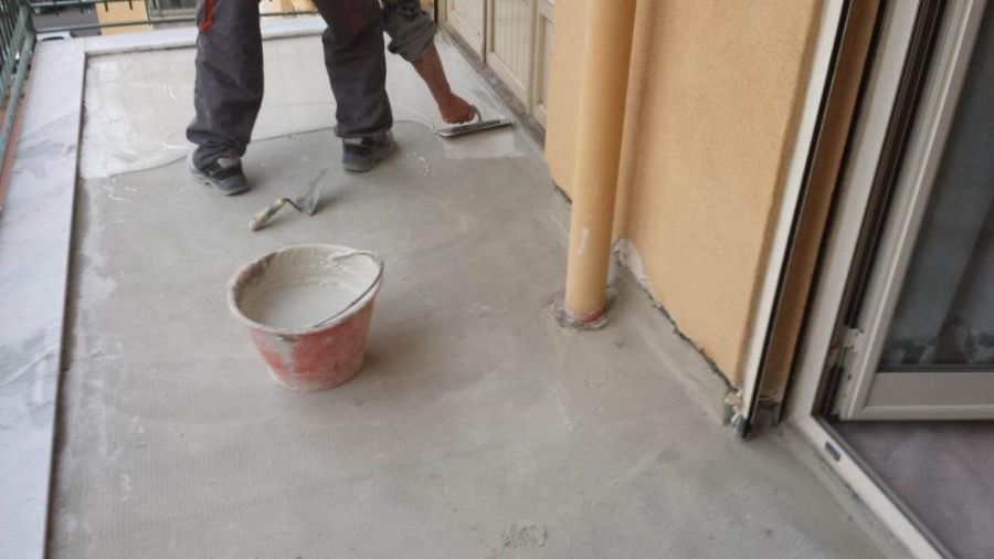 Persona che stende il cemento con una cazzuola su un balcone. Sul pavimento ci sono un secchio e degli attrezzi.