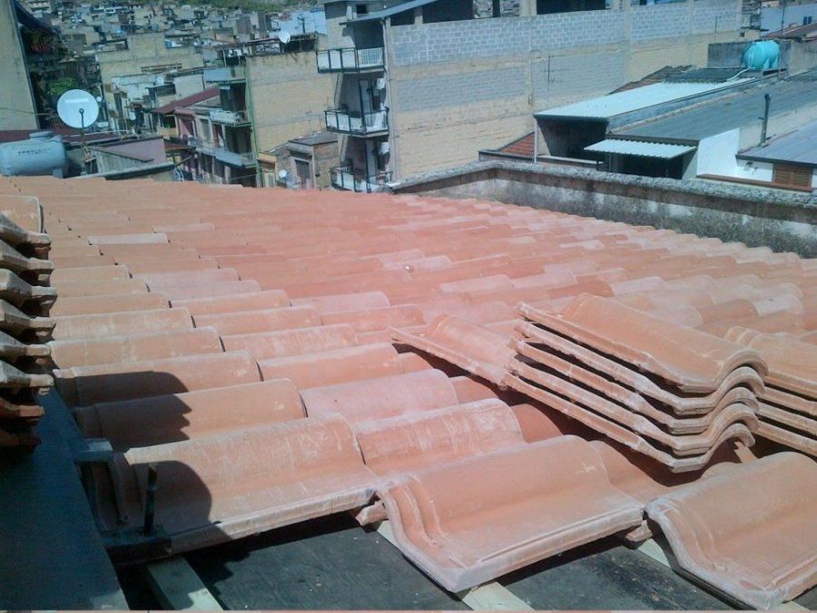 Tegole di argilla rossa posate su un tetto, con un paesaggio urbano visibile sullo sfondo.