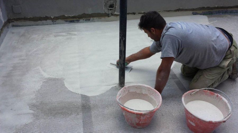 Uomo che applica sigillante bianco sul pavimento attorno a un tubo, con due secchi di sigillante.