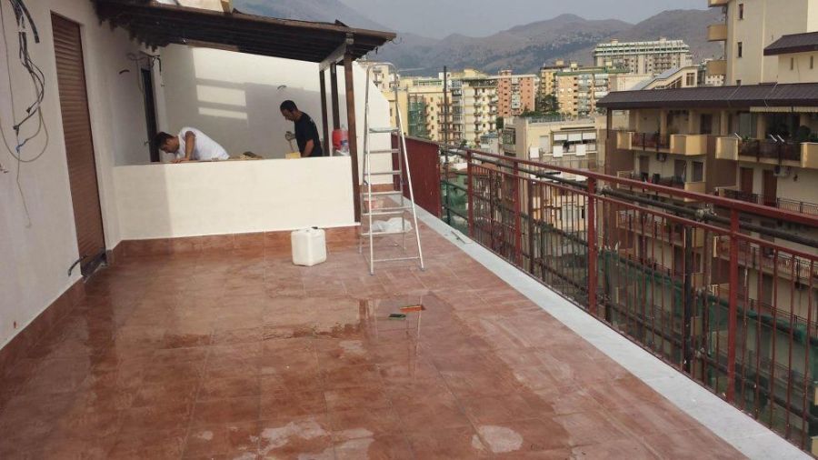 Operai che dipingono una terrazza sul tetto. Edifici e montagne sullo sfondo.