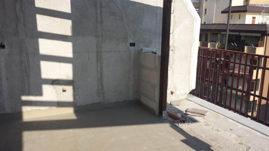 Stanza con pareti in cemento, ringhiera parziale in ferro e motivo a ombre, probabilmente in fase di costruzione o ristrutturazione.