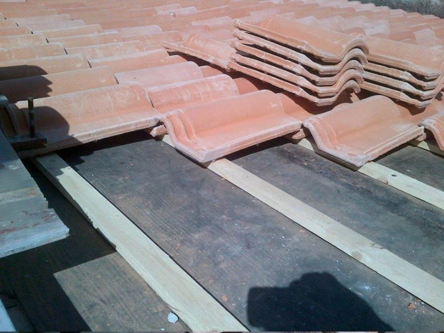 Tegole rosse in terracotta impilate su una struttura in legno, luce del sole.
