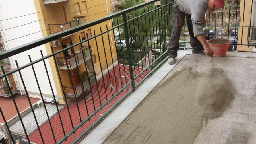 Persona che stende cemento sul pavimento di un balcone. Sono visibili un secchio e una ringhiera nera.