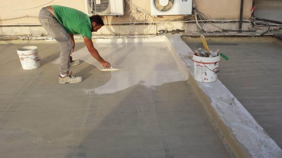 Persona che applica il sigillante su un tetto. Cemento grigio, sigillante bianco, maglietta verde, secchio.