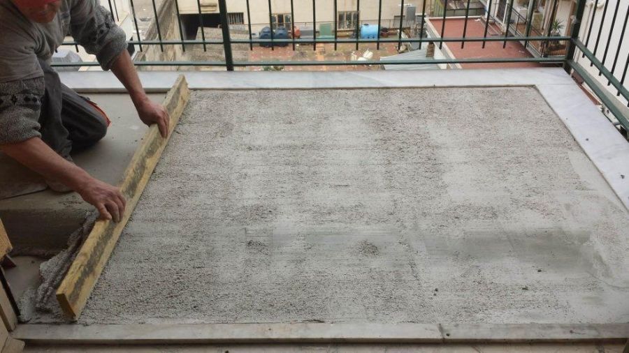 Persona che livella il cemento su un balcone con una tavola di legno; ambiente esterno.