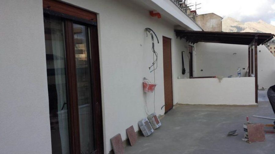 Esterno di un edificio con terrazza, infissi in legno e pavimento piastrellato.