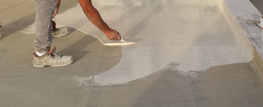 Una persona che usa una cazzuola per stendere una sostanza bianca su una superficie di cemento.