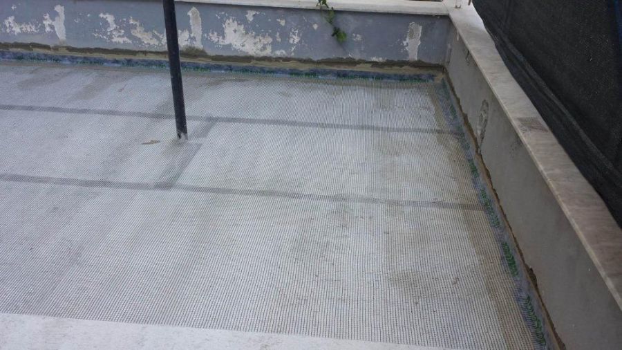 Un patio in cemento coperto da una rete a maglie grigie, con un palo nero al centro.