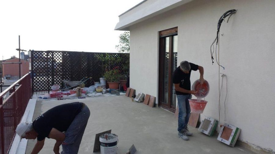 Due uomini lavorano su un muro esterno bianco. Uno versa il materiale da un contenitore, l'altro lavora sulle finiture.