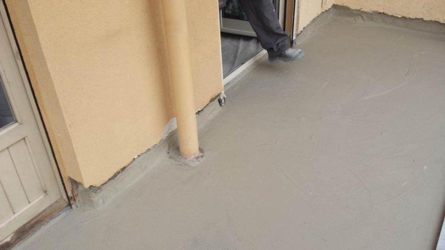 Una persona in piedi su una superficie di cemento grigio appena posata, vicino a un edificio.