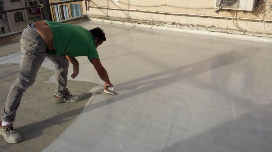 Uomo che applica sigillante bianco su un tetto con una cazzuola in una giornata di sole.