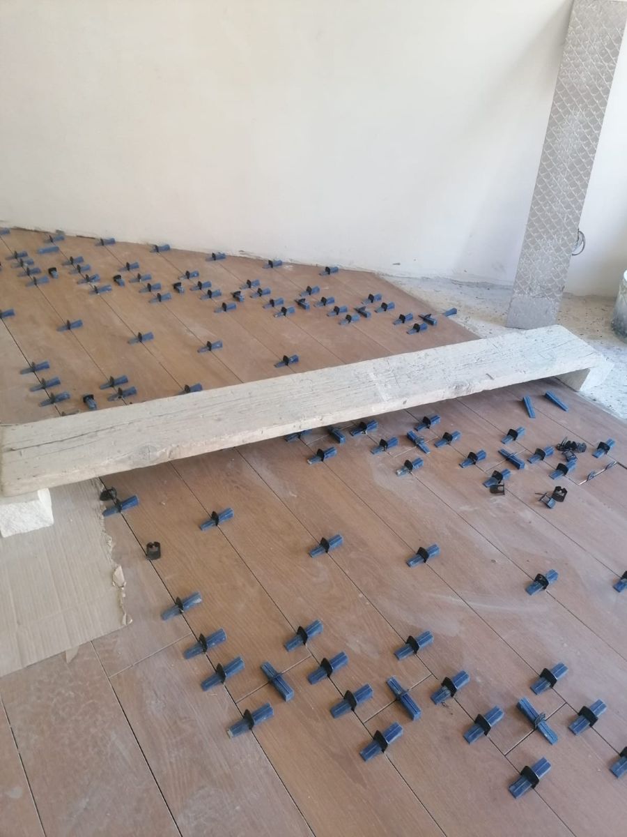 Installazione delle piastrelle del pavimento, con le clip di livellamento visibili. Come supporto viene utilizzata una tavola di legno.