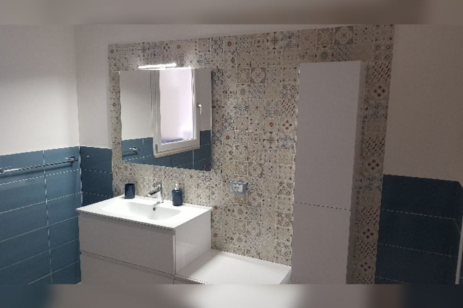 Bagno con lavandino e mobiletto bianchi, parete piastrellata blu, paraschizzi con piastrelle a fantasia e mobiletto alto bianco.