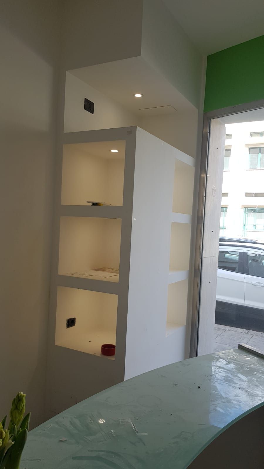 Mensole bianche integrate con illuminazione interna, accanto a una finestra e a un bancone curvo.