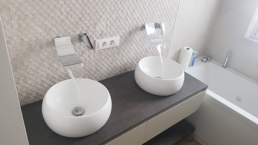 Due lavandini bianchi con rubinetti a cascata in un bagno moderno.