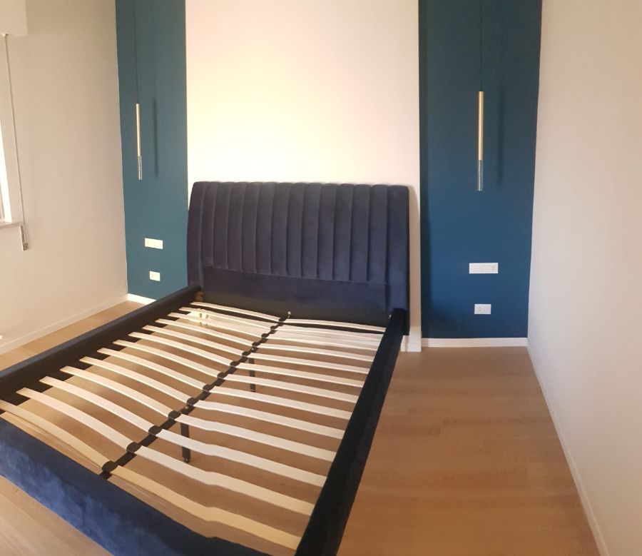 Camera da letto con testiera e struttura del letto blu, pavimento in legno chiaro e armadi color verde acqua su entrambi i lati.
