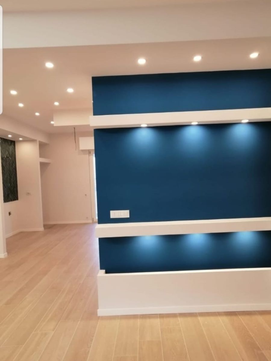 Parete decorativa blu con mensole e luci bianche integrate, in una stanza moderna con pavimento chiaro.