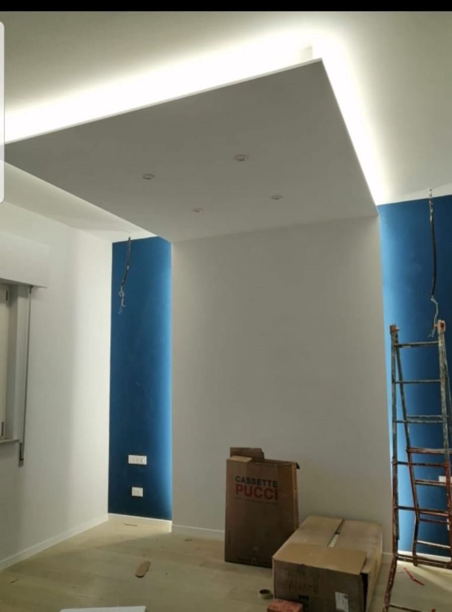 Stanza con soffitto incassato e pareti con dettagli blu. Sono presenti scatole di cartone e una scala.
