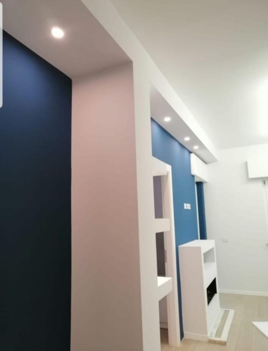 Interno con pareti blu e rosa, scaffalature bianche e illuminazione da incasso.