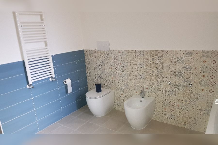 Bagno con piastrelle blu e fantasia, WC, bidet e portasciugamani.