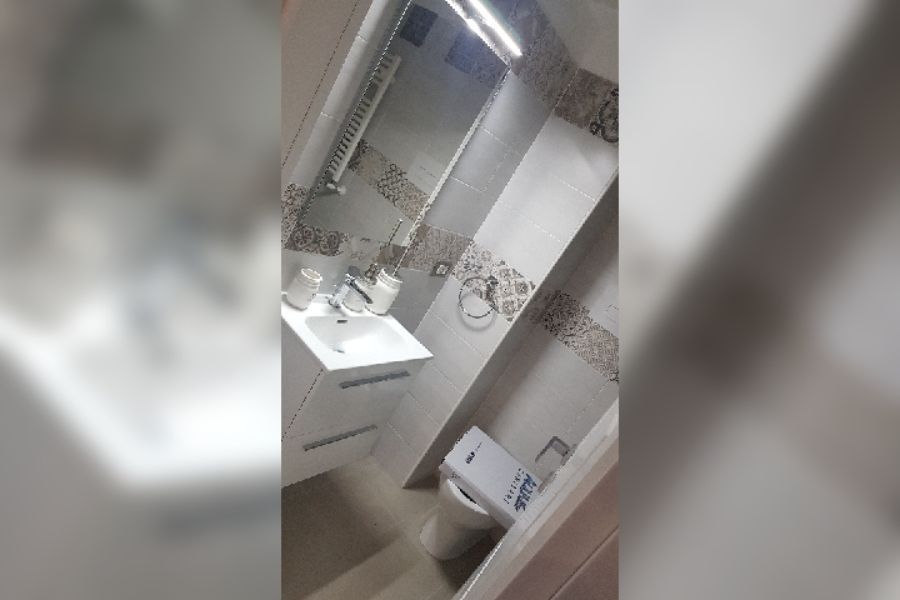 Bagno con lavandino bianco, WC, piastrelle beige e un grande specchio.