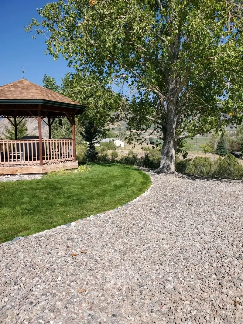 A gazebo is sitting in the middle of a lush green field next to a tree.