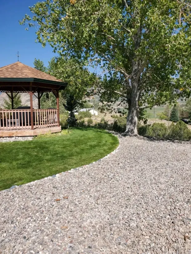 A gazebo is sitting in the middle of a lush green field next to a tree.