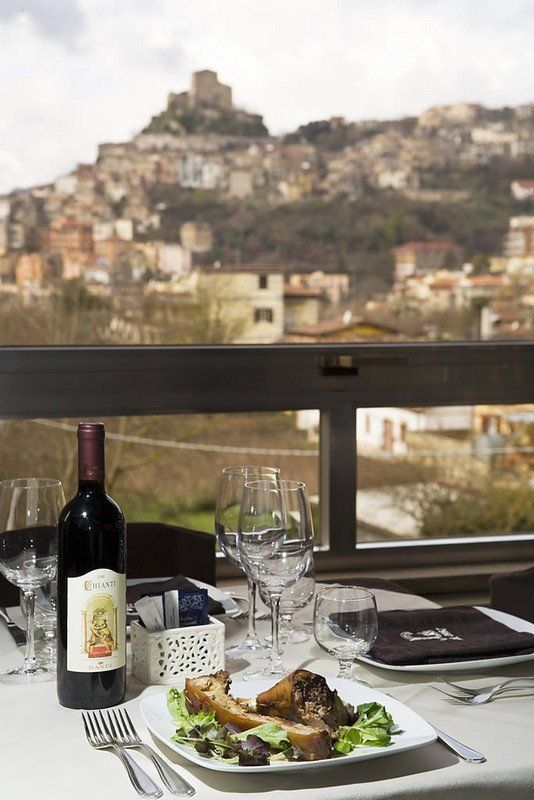 Tavolo del ristorante apparecchiato per cenare con una bottiglia di vino, cibo e la città sullo sfondo.