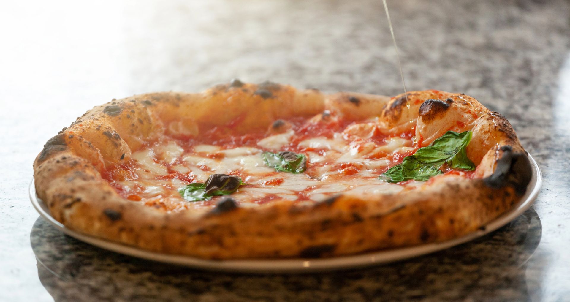 Pizza con salsa di pomodoro, mozzarella, basilico, su un piatto bianco, primo piano.