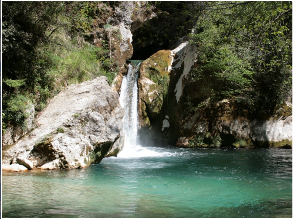 Cascata che si riversa in una piscina turchese, circondata da rocce e vegetazione lussureggiante.