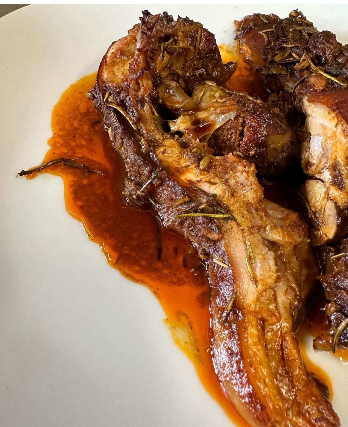 Carne brasata su un piatto bianco, con salsa rosso-arancio.