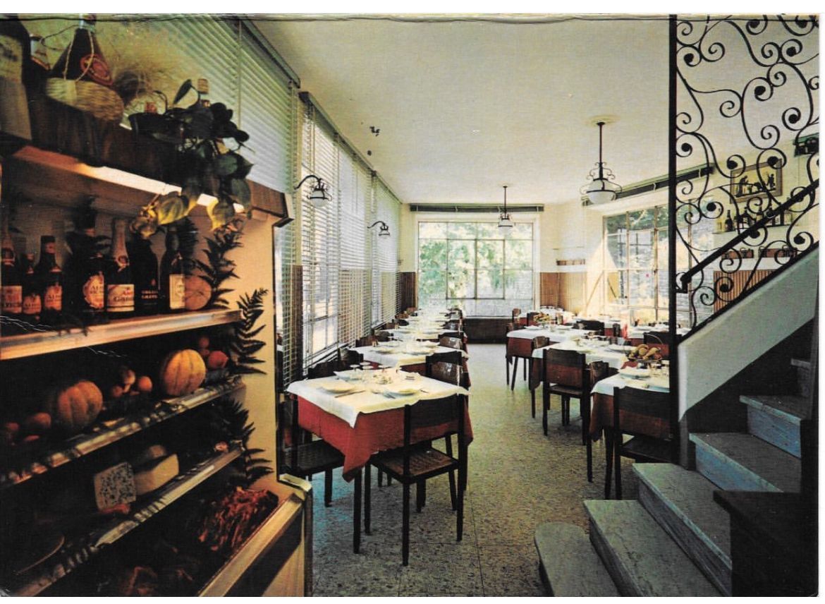 Interno di un ristorante con tavoli apparecchiati per mangiare, scaffali pieni di cibo e una scala.