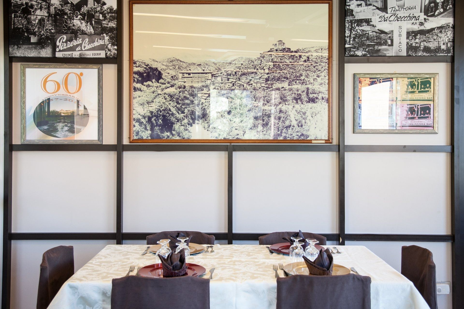 Tavolo da pranzo apparecchiato per quattro persone con quadri incorniciati alla parete. Decorazioni in bianco e nero con tovaglia e tovaglioli marroni.