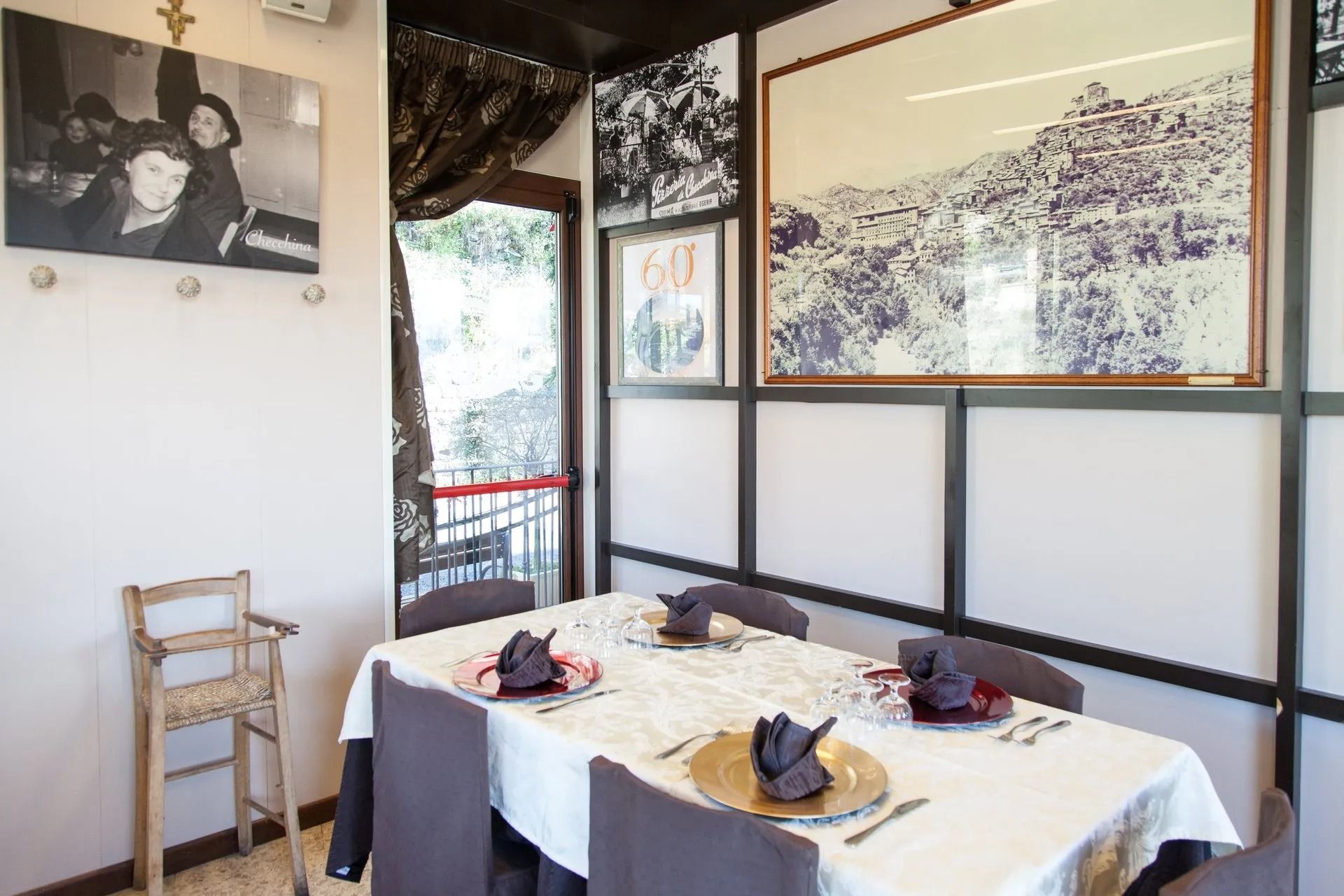 Sala da pranzo del ristorante con tavolo apparecchiato per quattro, decorato con opere d'arte e un seggiolone.