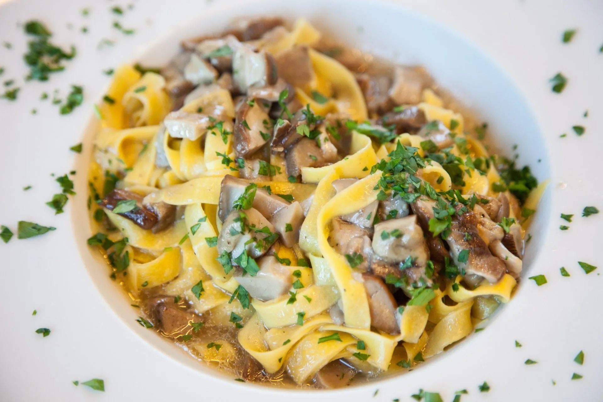 Piatto di pasta con tagliatelle, funghi e prezzemolo in una ciotola bianca.