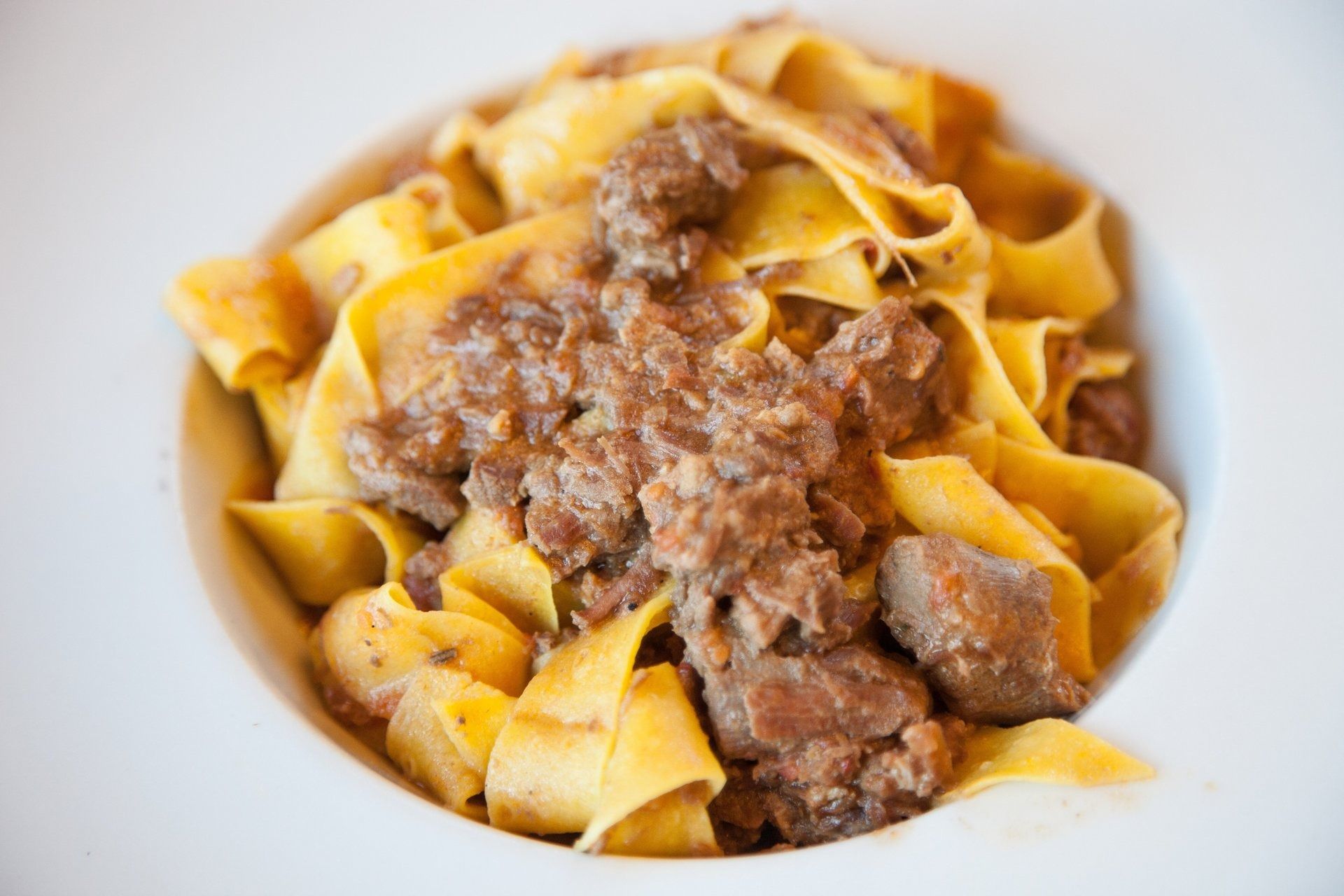 Pappardelle condite con un ricco sugo di carne in una ciotola bianca.